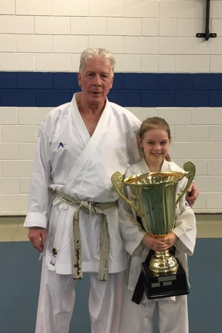 Sensei Fred Fawcett standing with Sophie when she was younger, Sophie is holding a karate trophy nearly as big as herself!